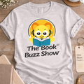 Gray t-shirt with 'The Book Buzz Show' logo on a wooden surface with coffee, glasses, and books.