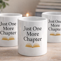 Three white mugs with 'Just One More Chapter' text on a wooden surface.